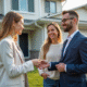 Agent immobilier souriant remettant les clés à un couple heureux devant une maison moderne