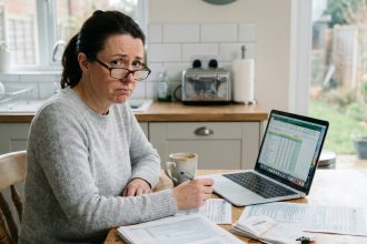 Femme en train de remplir sa déclaration d'impôt sur le revenu avec des documents de revenus locatifs étalés sur une table de cuisine